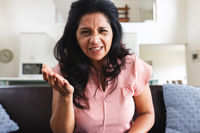 A woman in a pink shirt looking frustrated in a living room, relating to family and wealth issues.