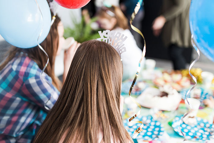 Woman at a birthday party with balloons and cake on the table.