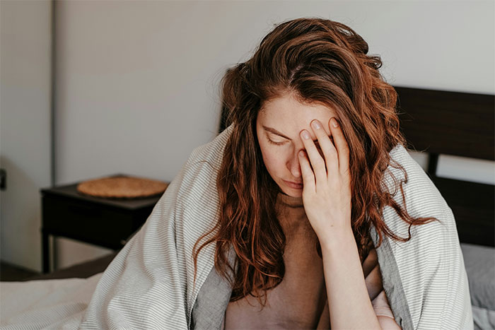 A tired woman under a blanket, hand on face, contemplating family issues.