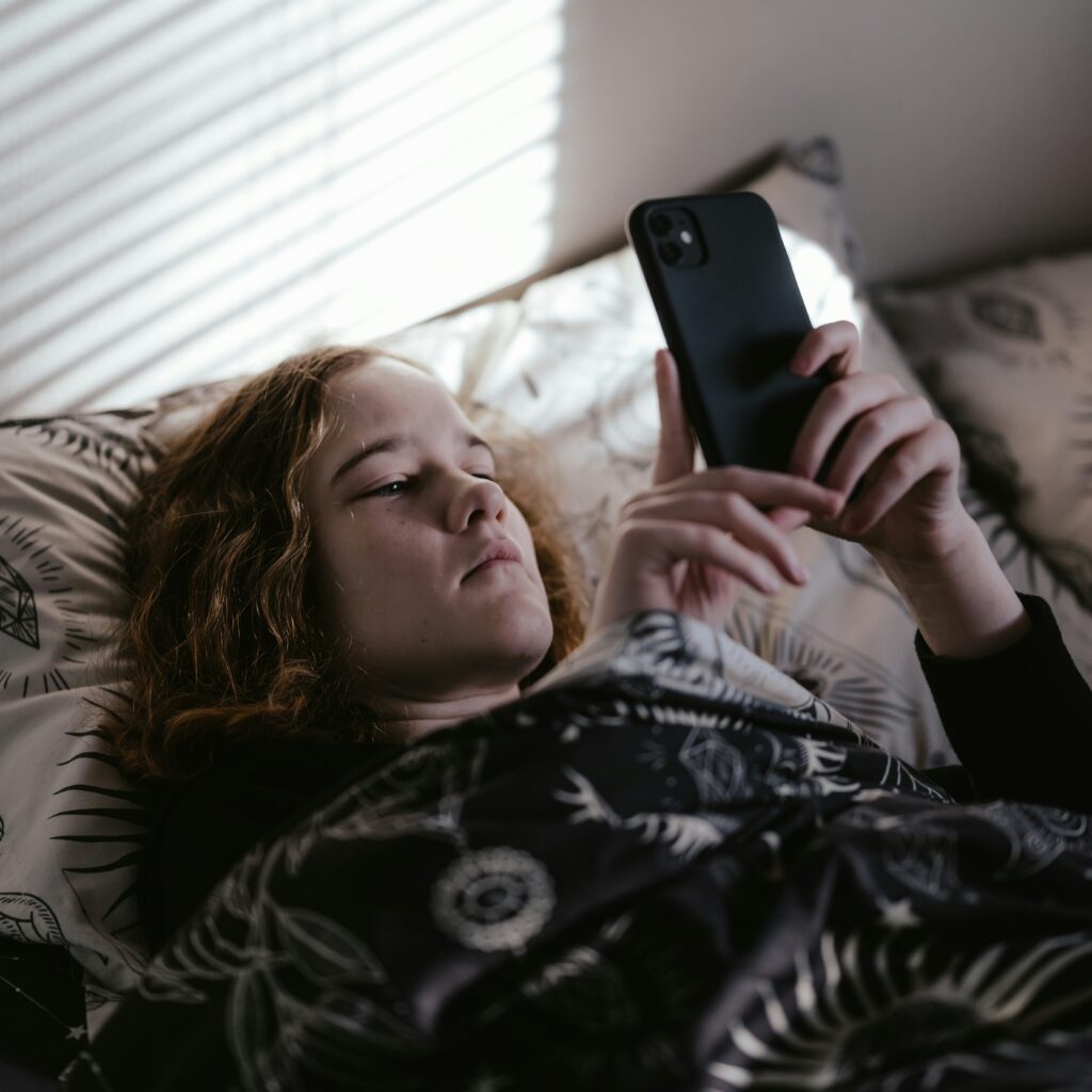 Person lying in bed, focused on a smartphone, under a patterned blanket with sun and moon designs.