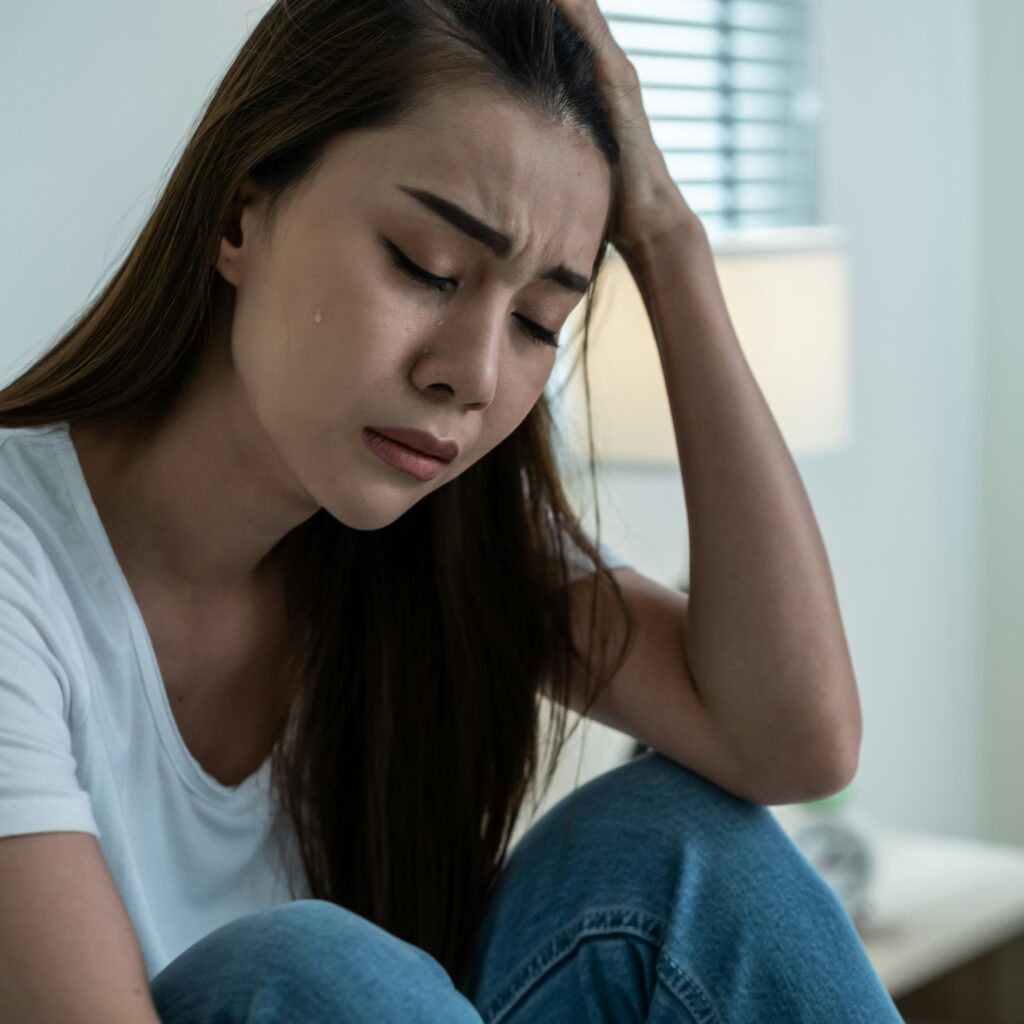 A woman in distress, sitting indoors, with tears on her face, symbolizing family chaos after affair revelation.