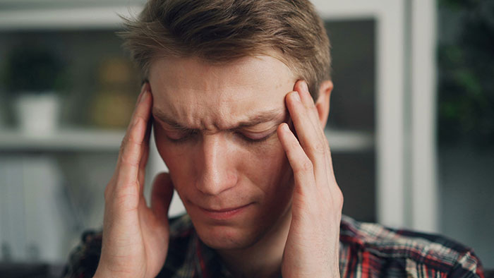 A guy with closed eyes, holding his temples, in a moment of care for his autistic cousin.