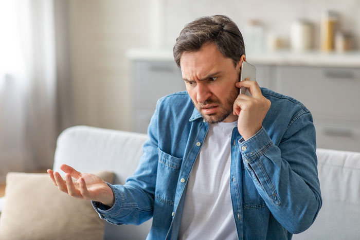 Man looking frustrated on a phone call, highlighting stereotypical school emergency call issues.
