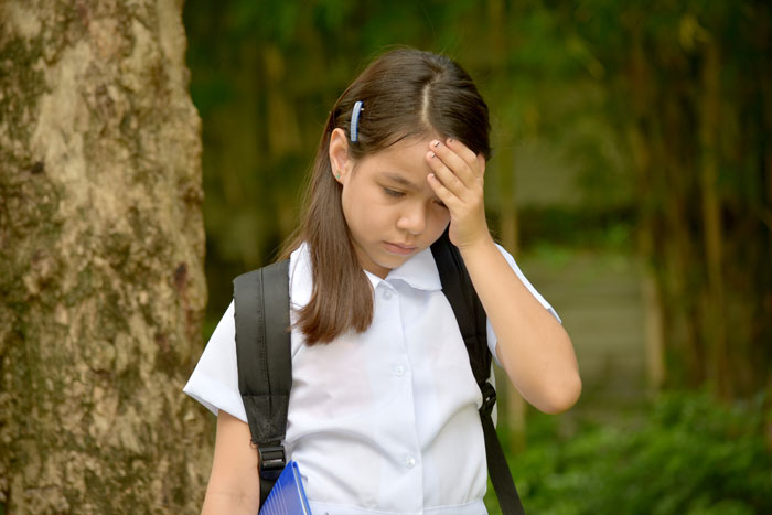 Young girl in school uniform looking upset outdoors, holding her head.