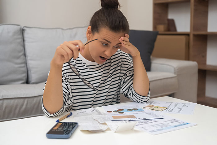 Woman reviewing late father’s estate documents looking stressed and overwhelmed while sitting in a living room.