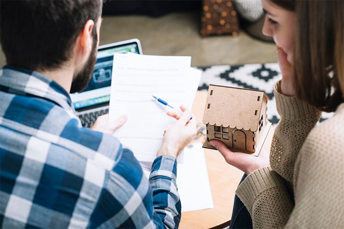 Couple reviewing estate documents while woman holds small wooden house model, reflecting on late father’s estate inheritance.