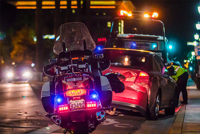 Police motorcycle and tow truck at night addressing accident involving a woman bearing physical consequences caused by fiancé.