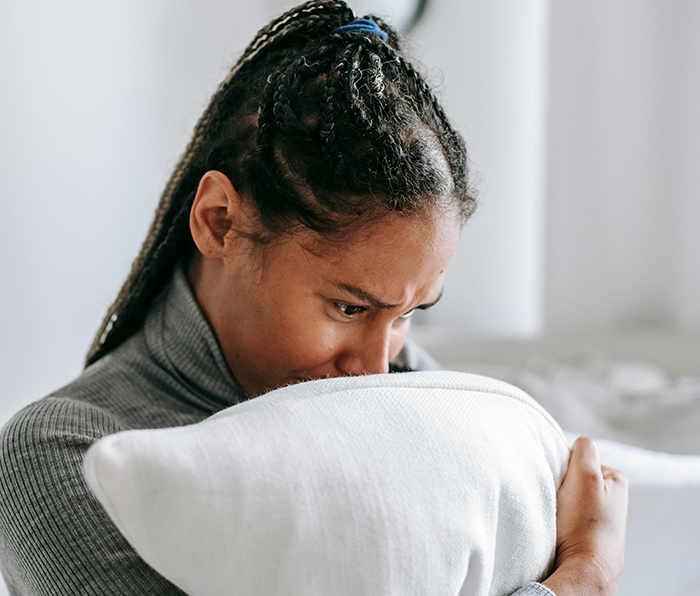 Woman hugging a pillow, looking upset while reflecting on choosing an affordable getaway over an expensive wedding event.