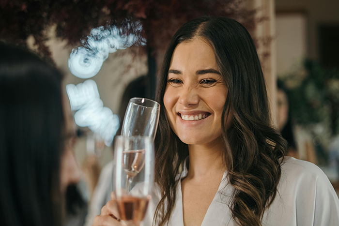Smiling woman holding a glass of champagne during a celebration, highlighting affordable getaway with husband over expensive wedding.